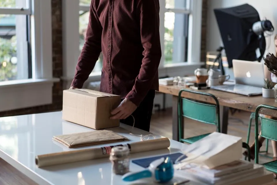 Seller packing an order into a cardboard box at a workspace